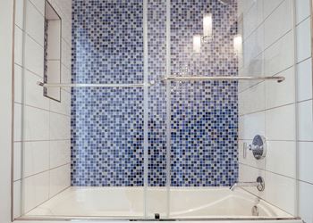 A shower with a blue tile wall and a white tub.